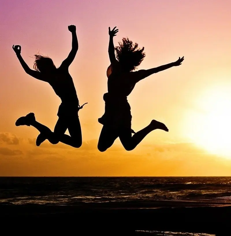 Zwei Frauen springen am Strand bei Sonnenuntergang in die Luft